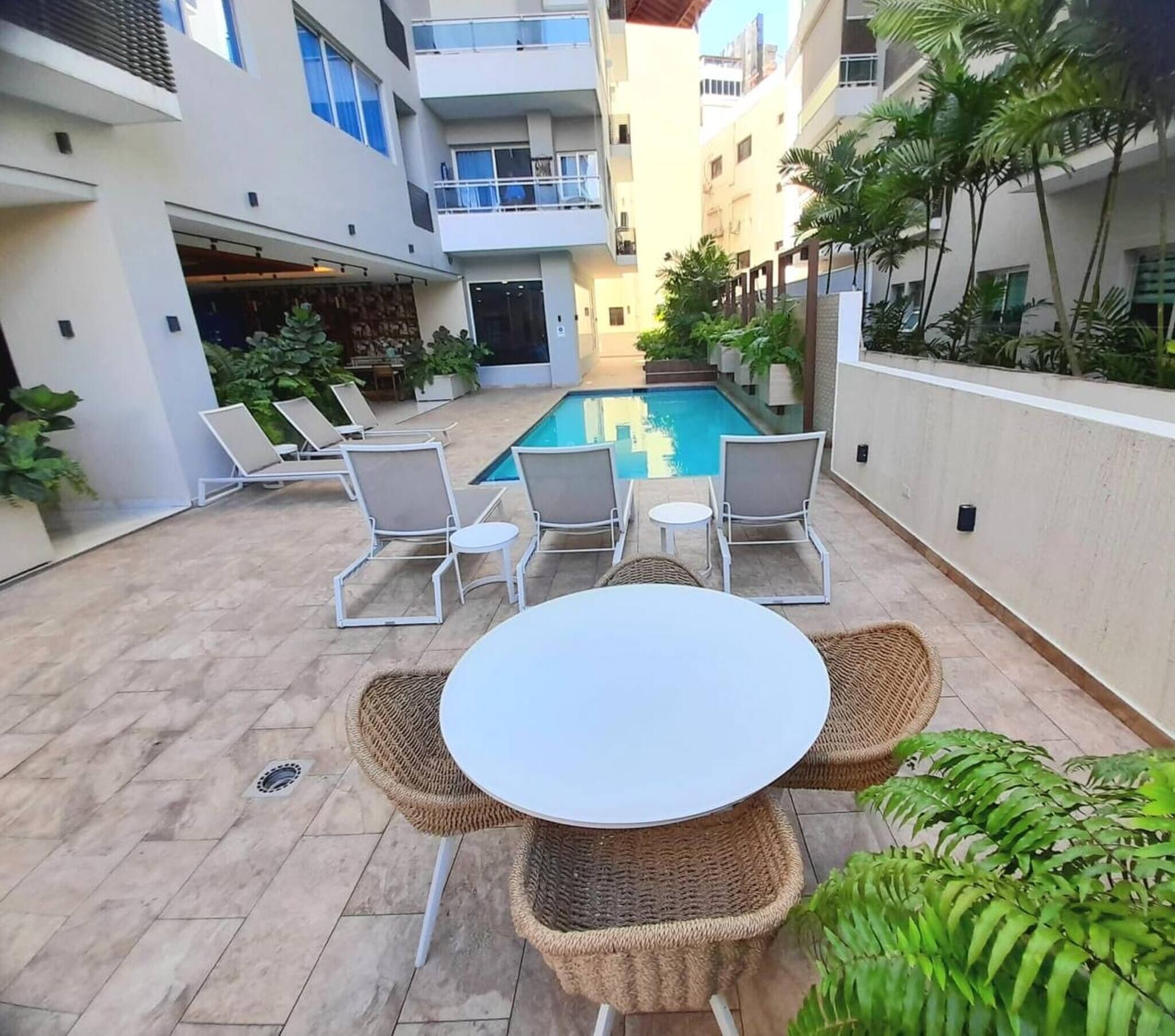An outdoor pool area with lounge chairs and a table, surrounded by buildings and greenery.
