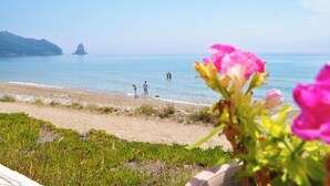 A beach with clear water, a distant island, and people walking along the shore. - Holiday House Letta Very Quiet Location Agios Gordios auf Korfu (Corfu)