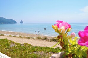 Ein Strand mit klarem Wasser, einer entfernten Insel und Menschen, die am Ufer entlanggehen.