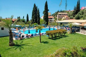 Ein Poolbereich mit Liegestühlen und Sonnenschirmen, umgeben von Grünflächen und Gebäuden.