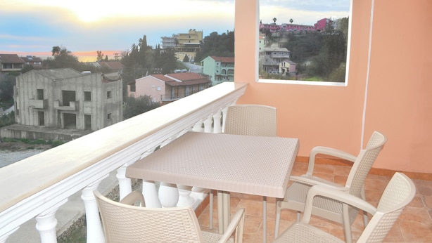 A balcony with a table and chairs, overlooking a residential area with buildings and a sunset view. - Holiday House Letta Very Quiet Location Agios Gordios auf Korfu (Corfu)