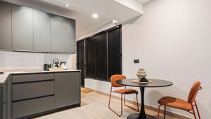 Une cuisine moderne avec des meubles gris, un îlot central noir et une table de salle à manger ronde, accompagnée de deux chaises orange.