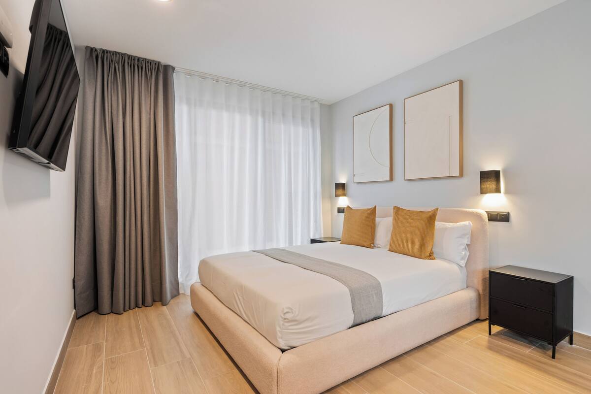 Une chambre moderne avec un grand lit, une table de chevet et un téléviseur à écran plat fixé au mur.