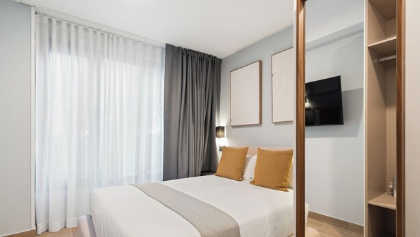 Une chambre d’hôtel moderne avec un grand lit, un téléviseur fixé au mur et un plancher en bois.