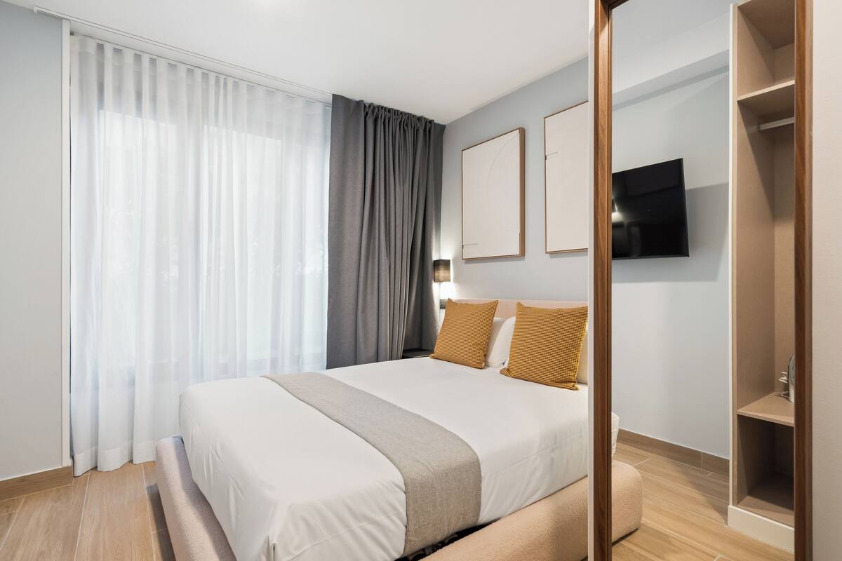 Une chambre d’hôtel moderne avec un grand lit, un téléviseur fixé au mur et un plancher en bois.