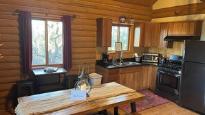 A cozy cabin-style kitchen with wooden walls, a dining table with a 'Welcome' sign, a stove, a sink, and a refrigerator.