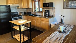Una cocina con armarios de madera, un refrigerador negro, una estufa, un microondas, una cafetera y una pequeña mesa con una vela.