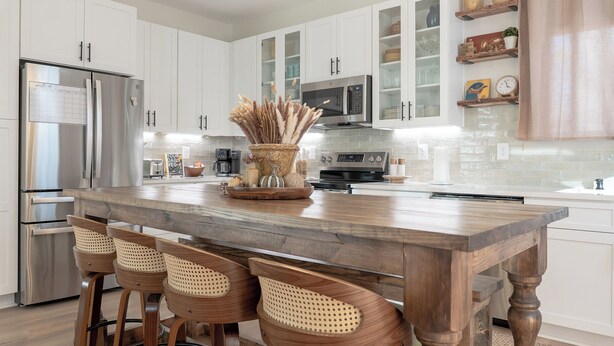 A modern kitchen with white cabinets, stainless steel appliances, and a wooden island with bar stools. - Cozy New House in a Prime Location (Carrollton)