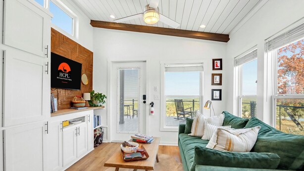 A spacious living room with a green sofa, wooden coffee table, and a television mounted on a white wall. - Secluded Hill Country Ranch on 105 Acres Near Pedernales State Park (Johnson City)