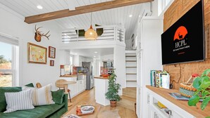 A spacious living area with a green sofa, a coffee table with books, a small Christmas tree, and a mounted deer head. - Secluded Hill Country Ranch on 105 Acres Near Pedernales State Park (Johnson City)