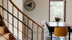 A modern interior with a wooden staircase, a dining area with a table and chairs, and a wall clock.