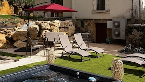 A pool with lounge chairs and a red umbrella, a stone wall, and a building with a tiled roof.