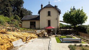 A two-story building with a stone facade, a red umbrella, and a pool area.