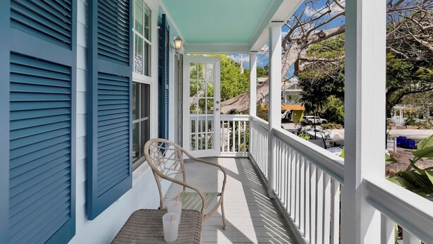 A covered porch with a wicker chair, a white railing, and a view of the neighborhood. - **WINDWARD WAVES @ OLD TOWN** Cottage by Duval + Last Key White Glove Service... (Key West)