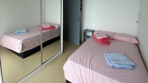 Una habitación con dos camas, un ventilador de techo, un espejo y una puerta.