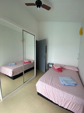 A room with two beds, a ceiling fan, a mirror, and a door. - Beachfront house with pool next to the Sesc Cacupe hotel. (Florianópolis)