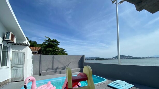 Una piscina en la azotea con un flotador de flamenco rosa y un tobogán amarillo, con vistas a una masa de agua y tierra a lo lejos.