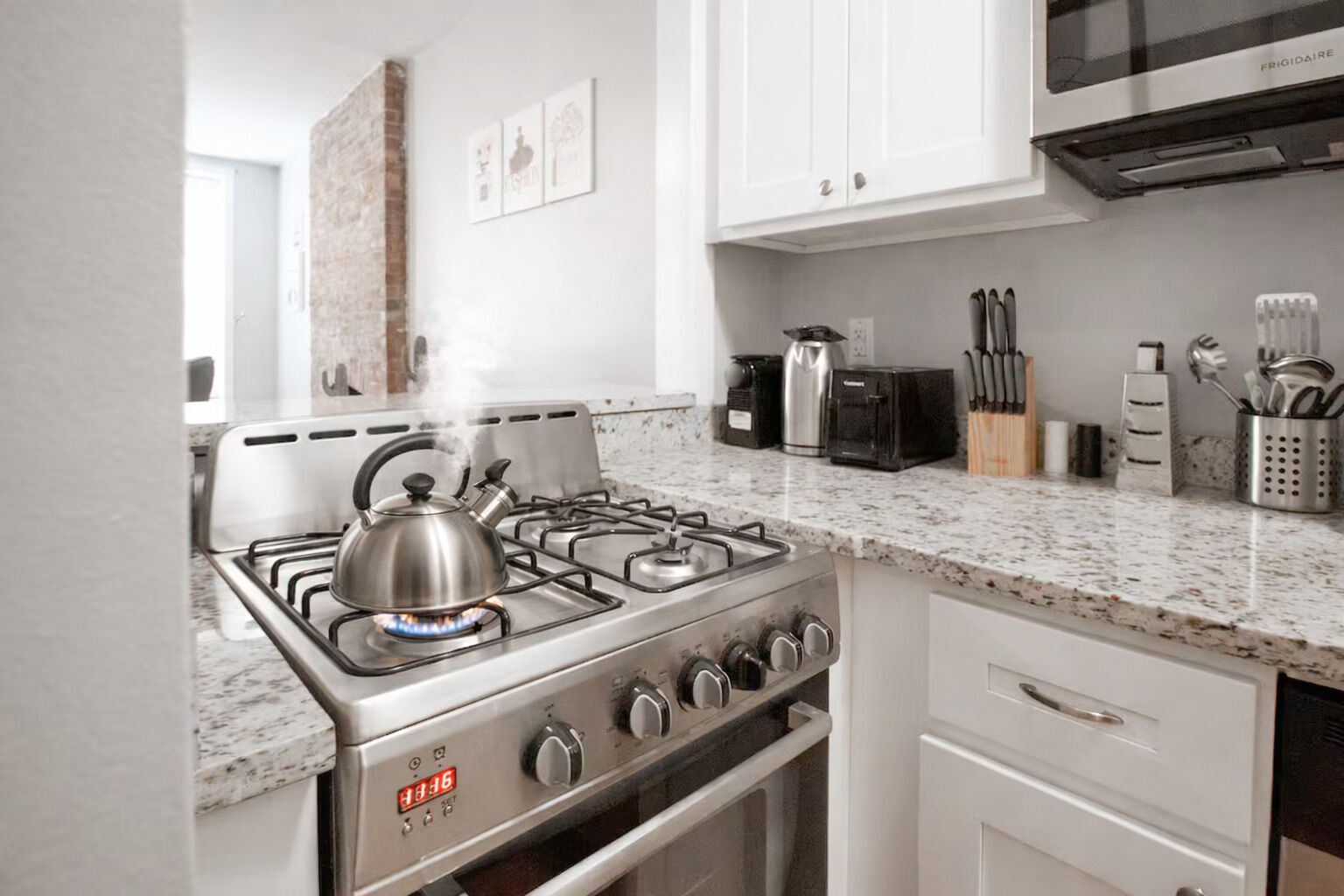 A modern kitchen with a gas stove, a kettle, a toaster, and various utensils on the countertop.