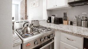 Una cocina moderna con estufa a gas, tetera, tostadora y diversos utensilios sobre la encimera.