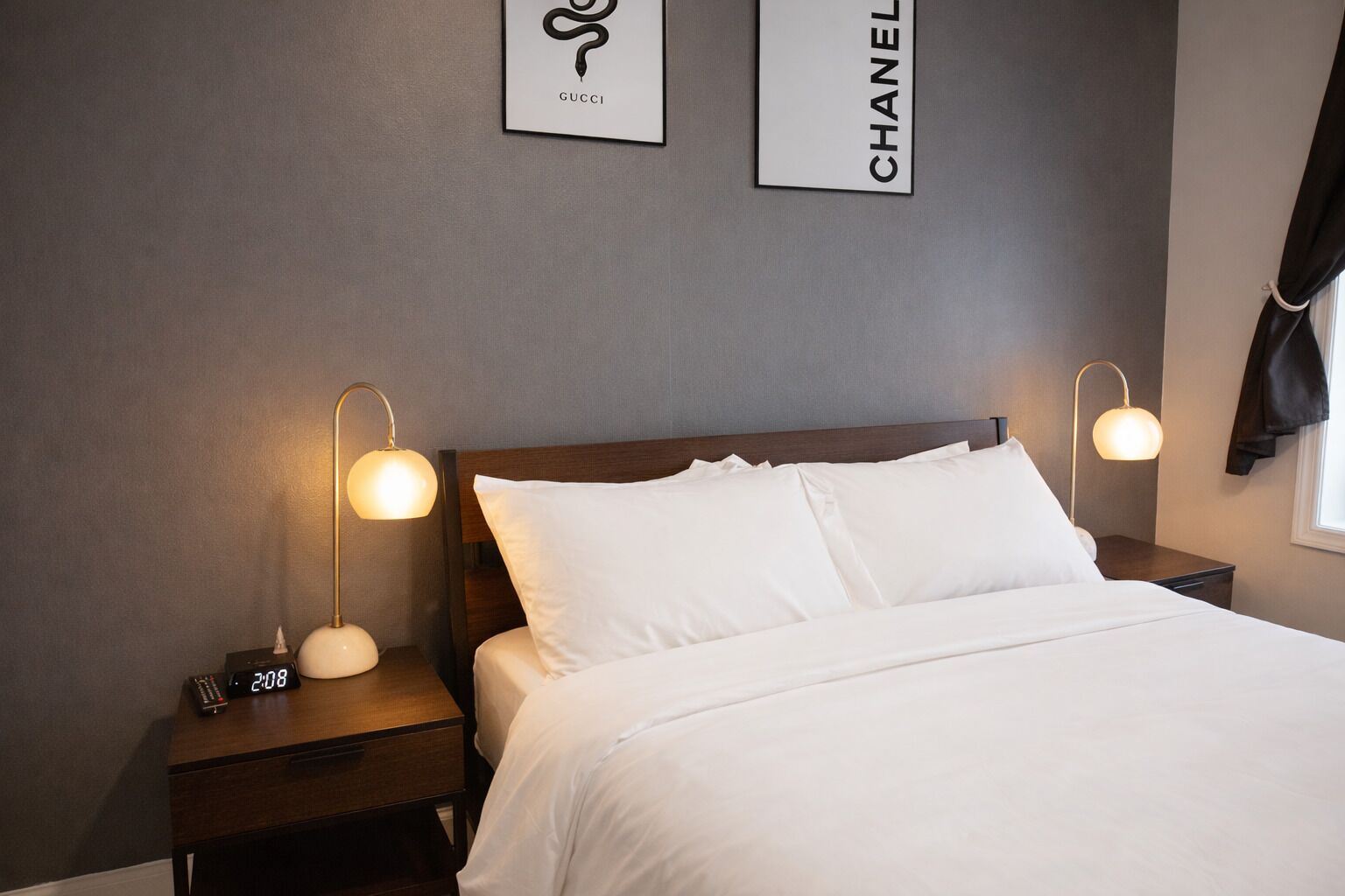 A hotel room with a neatly made bed, two bedside tables with lamps, and two framed logos on the wall.