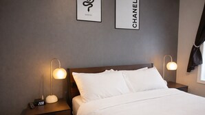 Una habitación de hotel con una cama bien hecha, dos mesitas de noche con lámparas, y dos logotipos enmarcados en la pared.