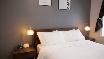 A hotel room with a neatly made bed, two bedside tables with lamps, and two framed logos on the wall.