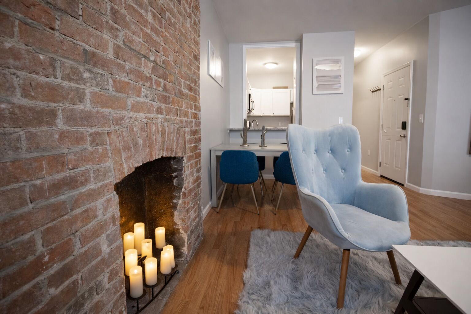 A modern living room with a brick fireplace, a dining area with blue chairs, and a light blue armchair.