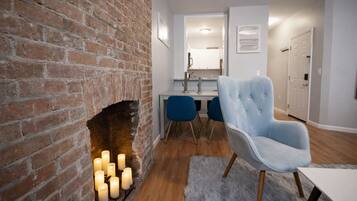 A modern living room with a brick fireplace, a dining area with blue chairs, and a light blue armchair.