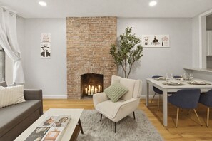 Een moderne woonkamer met een metselstenen open haard, een eethoek met een tafel gedekt voor twee personen, en een gezellige zithoek.