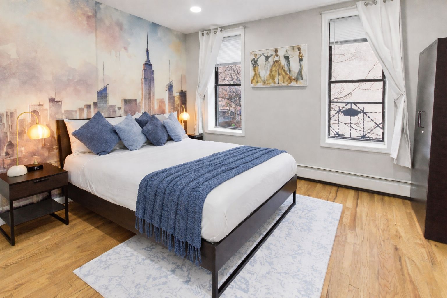 Een slaapkamer met een bed, nachtkastjes, een stadslandschap op de muur en een raam met gordijnen.