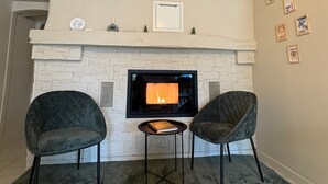 A fireplace with a stone facade, two upholstered chairs, a small table, and a framed picture above the fireplace. - LE CHALET DES PINS (Clermont)