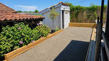 A gravel pathway leading to a building with a tiled roof, surrounded by wooden raised beds with green plants.