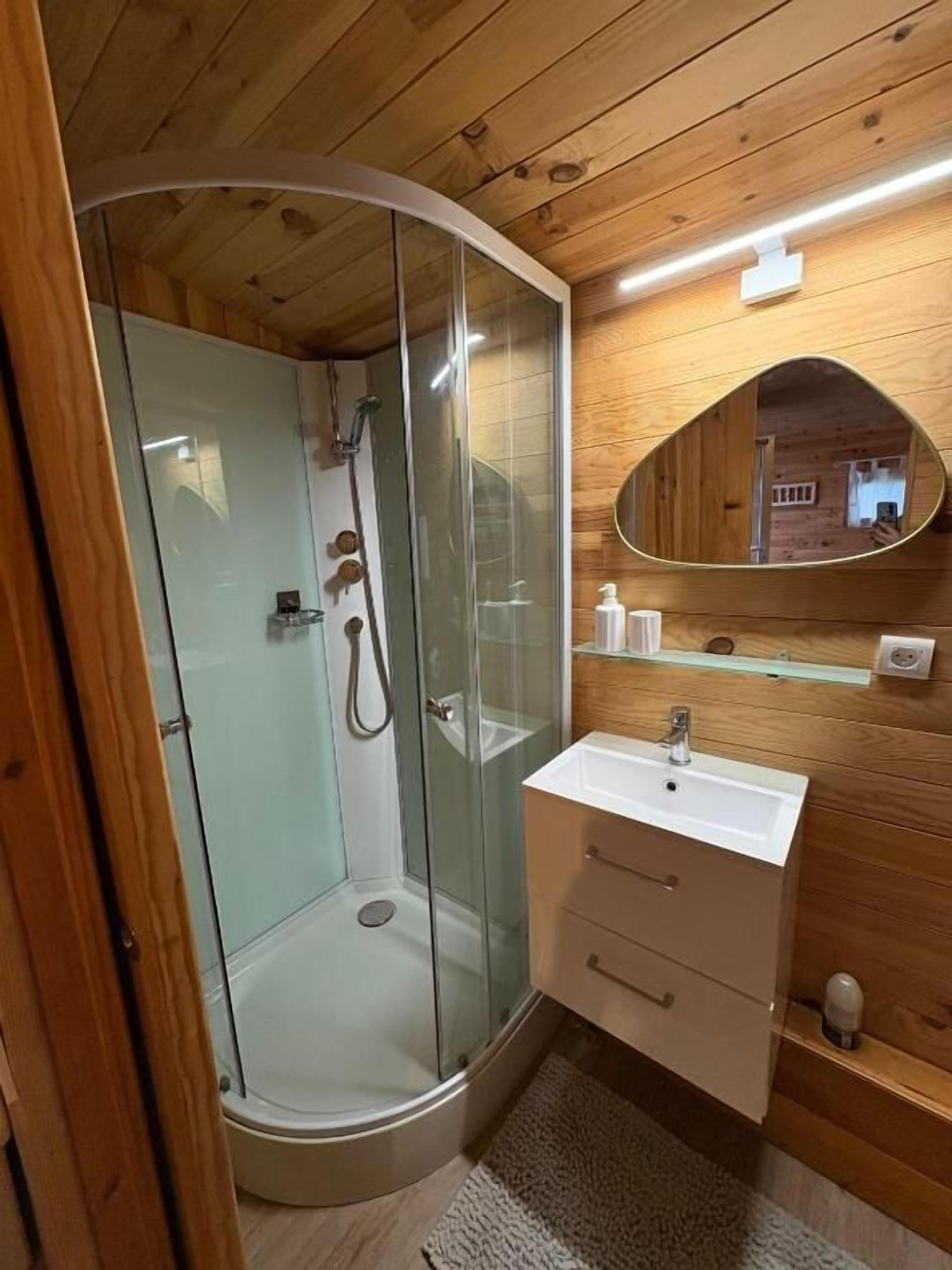 Une salle de bain rustique, avec une cabine en bois, une douche en verre, un lavabo et un miroir.