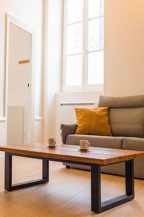 A modern living room with a wooden coffee table, a sofa with a yellow pillow, and a window with natural light. - Le Refuge de l'Arquebuse (Dijon)