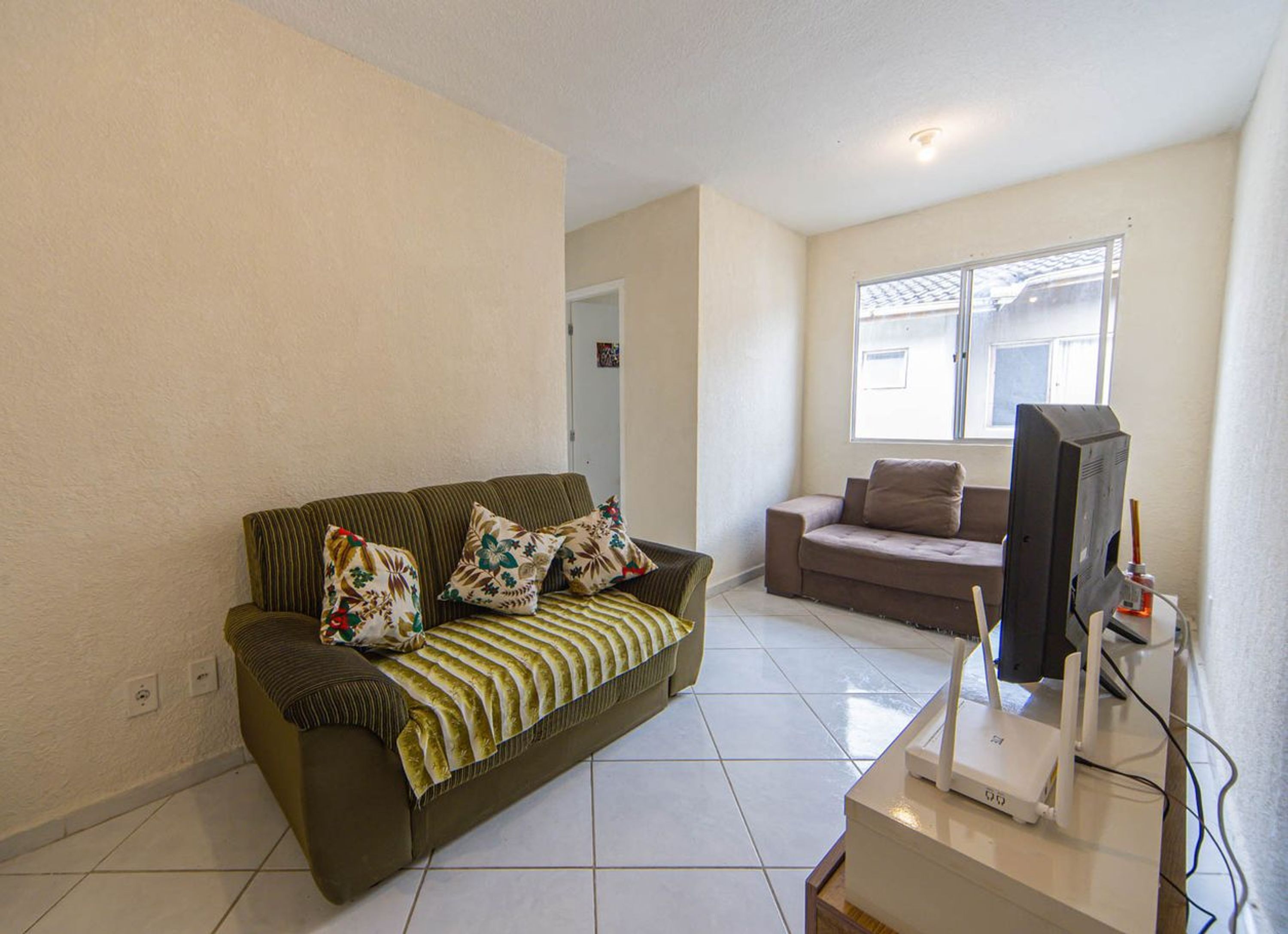 Uma sala de estar com sofá, televisão e janela.