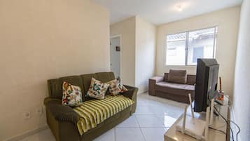 Uma sala de estar com sofá, televisão e janela.