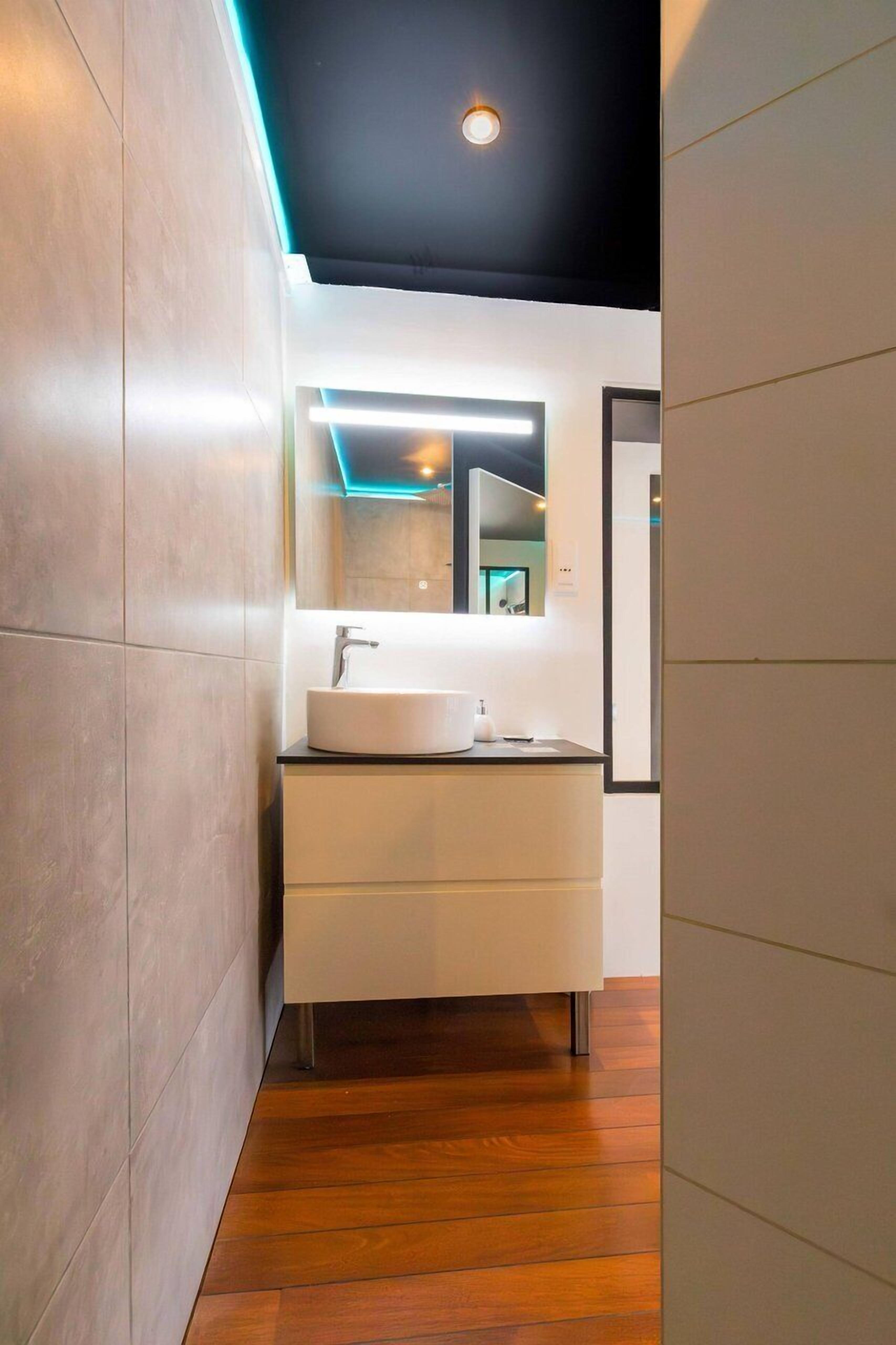 Een moderne badkamer met een witte wastafel, spiegel en houten vloer.