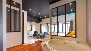 A modern bathroom with a large bathtub, wooden flooring, and large windows. - 🛁 Balnéo Suite Arquebuse — Love'appart & Jacuzzi (Dijon)