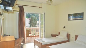 A hotel room with two single beds, a desk, a chair, and a balcony with a view of trees and buildings. - Holiday House Letta in a Very Quiet Location in Agios Gordios Beach, Corfu (Corfu)