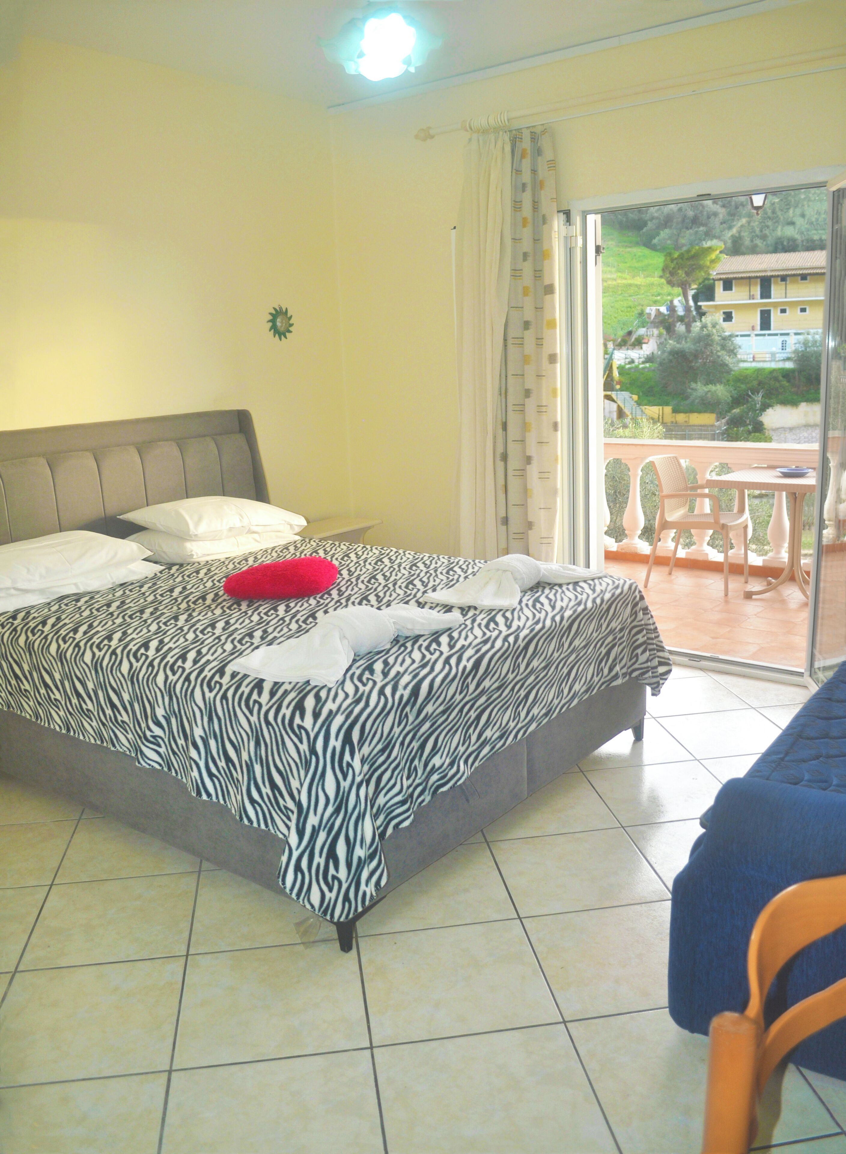 Un dormitorio con colcha de estampado de cebra, almohada roja y vistas a un balcón con mobiliario exterior.