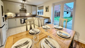 A modern kitchen with white cabinets, a dining table set for six with plates, cutlery, and wine glasses. - 4 Bed | Free Parking | Fast WiFi | Desk | Pets (Buckshaw Village)