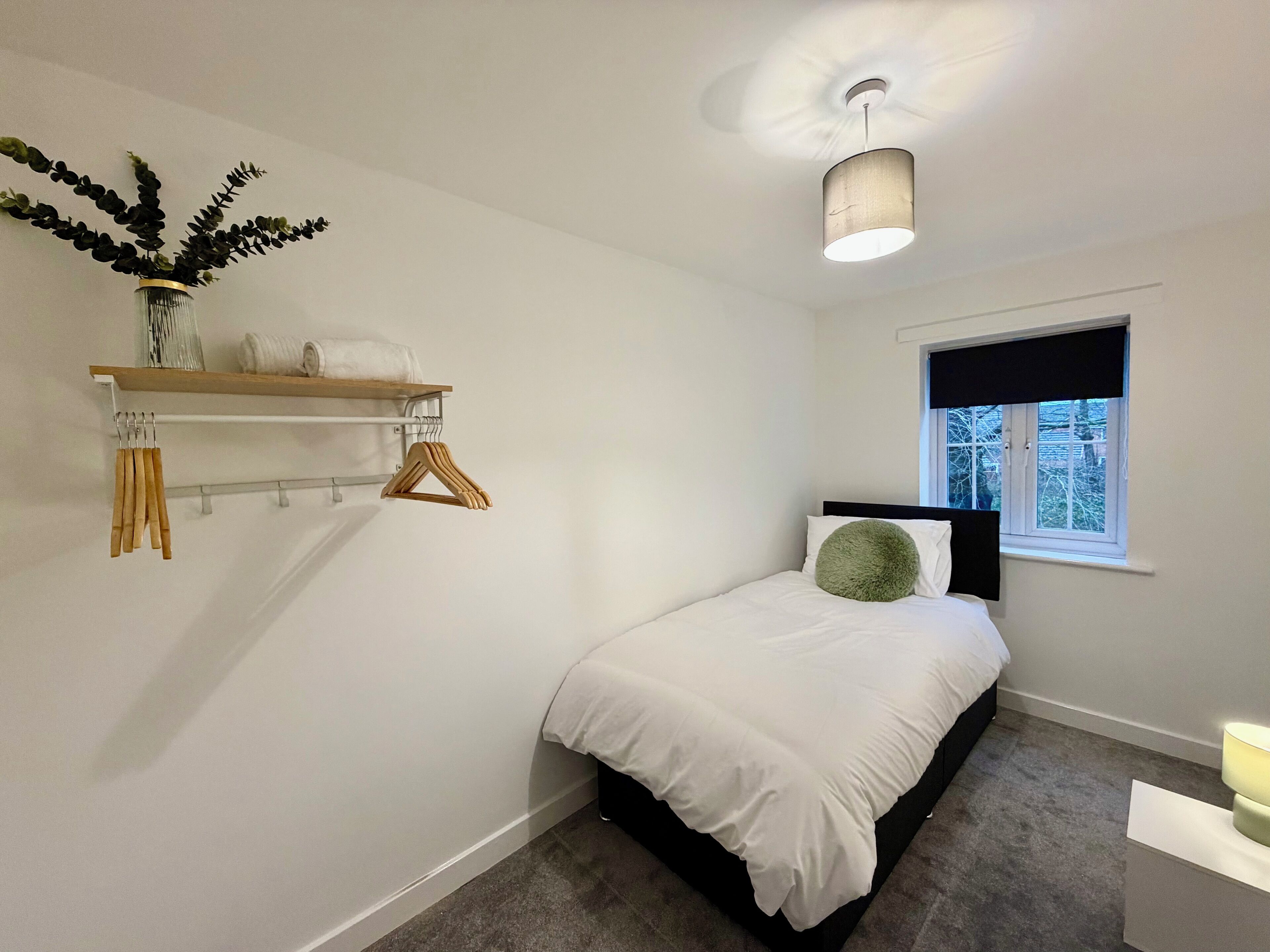 Ein Schlafzimmer mit einem Bett, einem Fenster, einer hängenden Pflanze und einem Deckenventilator.