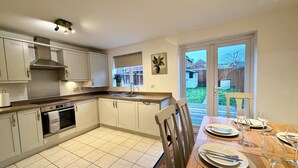 A modern kitchen with white cabinets, a built-in oven, and a dining area with a wooden table set for four. - 4 Bed | Free Parking | Fast WiFi | Desk | Pets (Buckshaw Village)