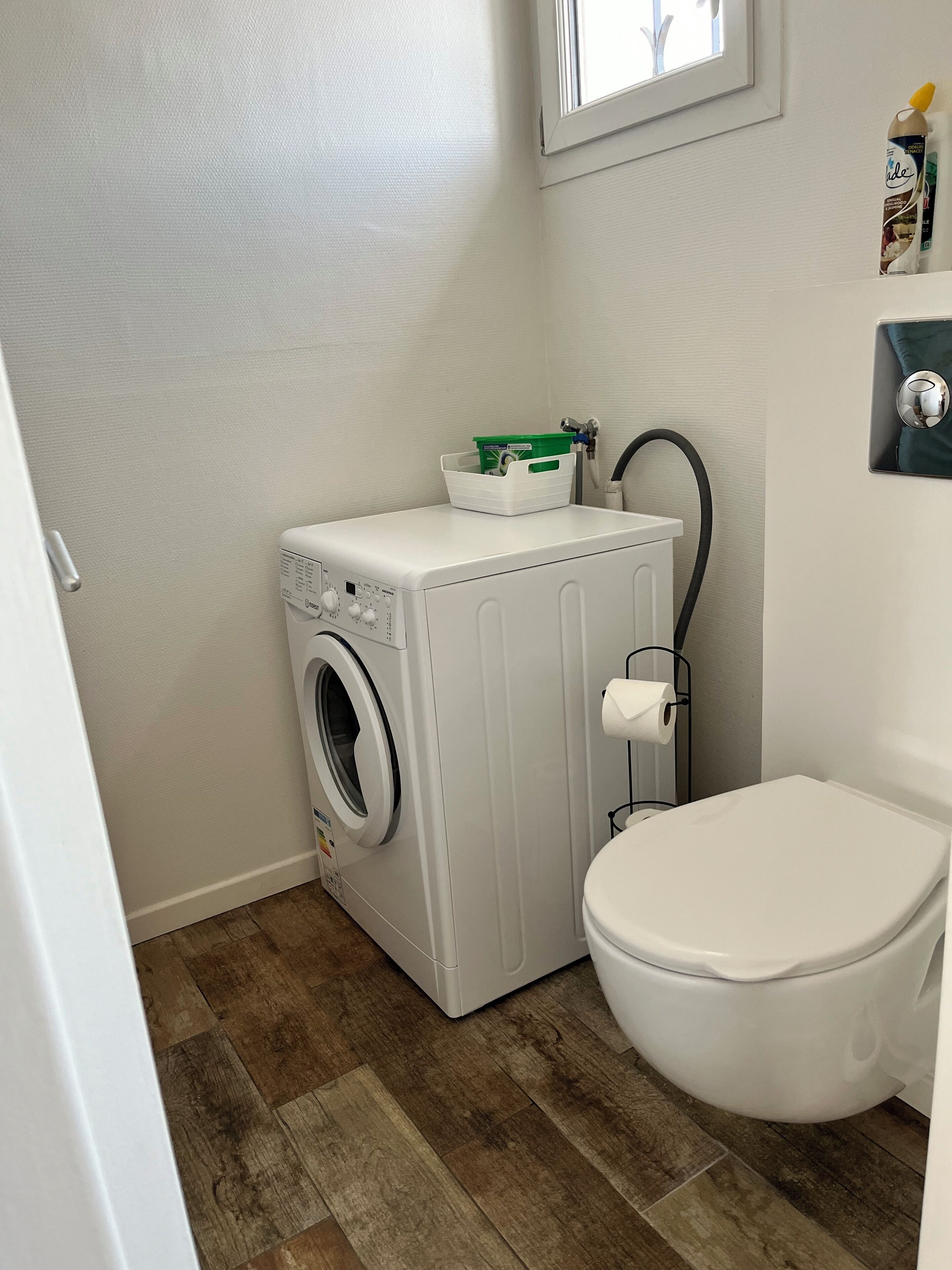 Ett litet badrum med tvättmaskin, toalett och ett litet fönster.