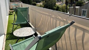 En balkon med grønne stole og et bord, med udsigt over et boligområde med huse og træer.