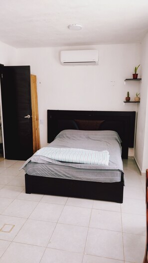 A bedroom with a bed, a door, a wall-mounted air conditioner, and a shelf with plants. - Depa  Tren Maya y Facultades UAC Ing /Qfb Periférico  Pet Friendly  CAMPECHE (San Francisco de Campeche)