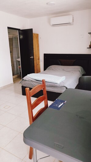 A room with a bed, a table, a chair, an air conditioning unit, and a door leading to a bathroom. - Depa  Tren Maya y Facultades UAC Ing /Qfb Periférico  Pet Friendly  CAMPECHE (San Francisco de Campeche)