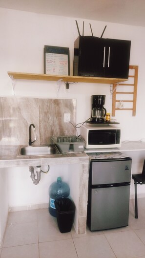 A compact kitchen with a sink, a small refrigerator, a microwave, a coffee maker, and a water dispenser.