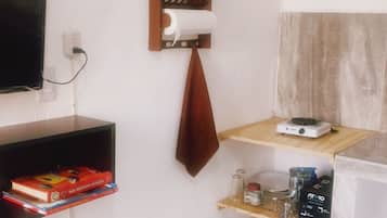 Una piccola cucina ben organizzata con un forno a microonde, uno scaffale con libri, una pianta in vaso e diversi utensili da cucina.