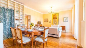 Un comedor con mesa y sillas de madera, una araña y un sofá al fondo.